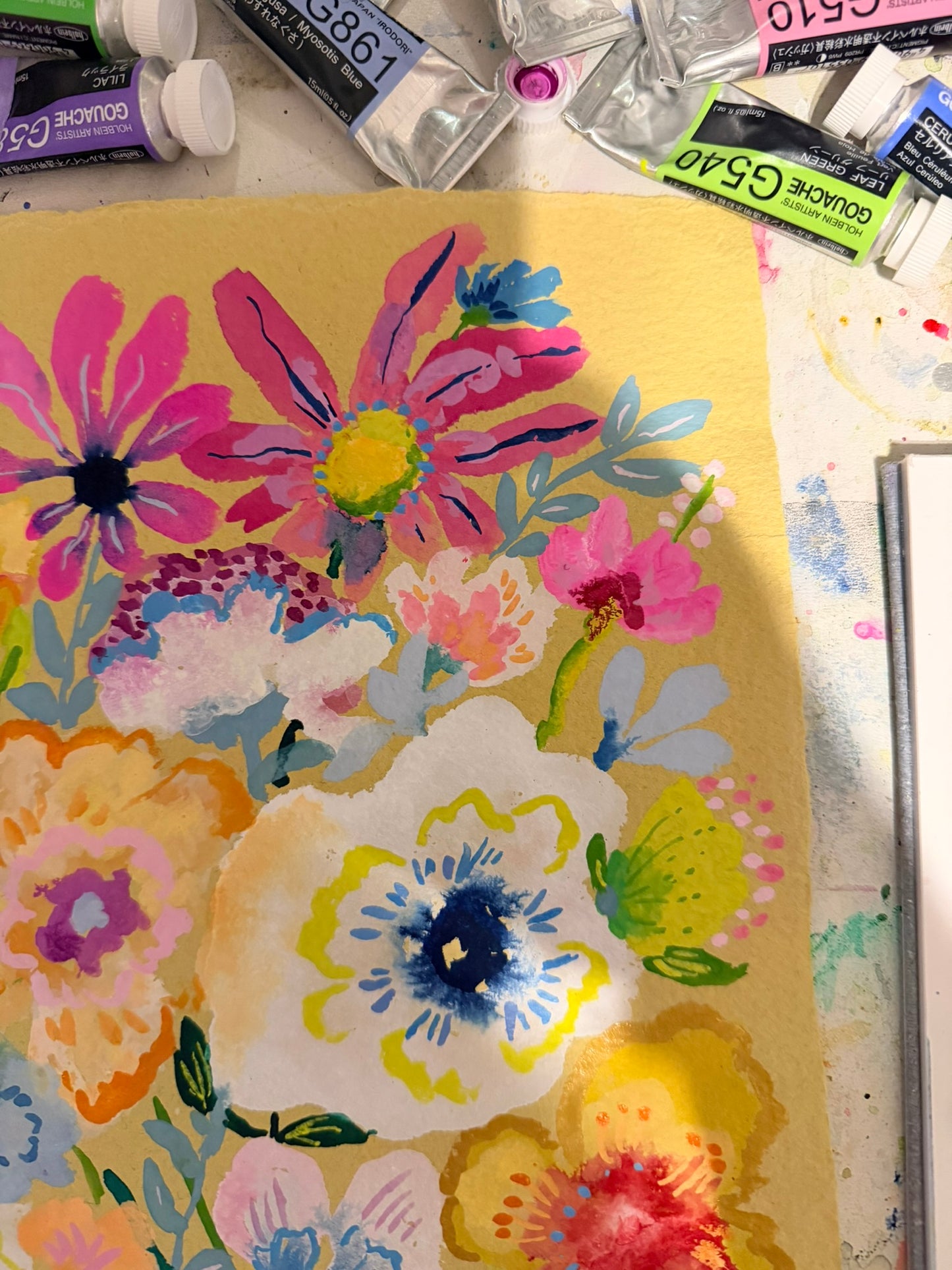 Colorful floral painting on a yellow background with art supplies in the background.