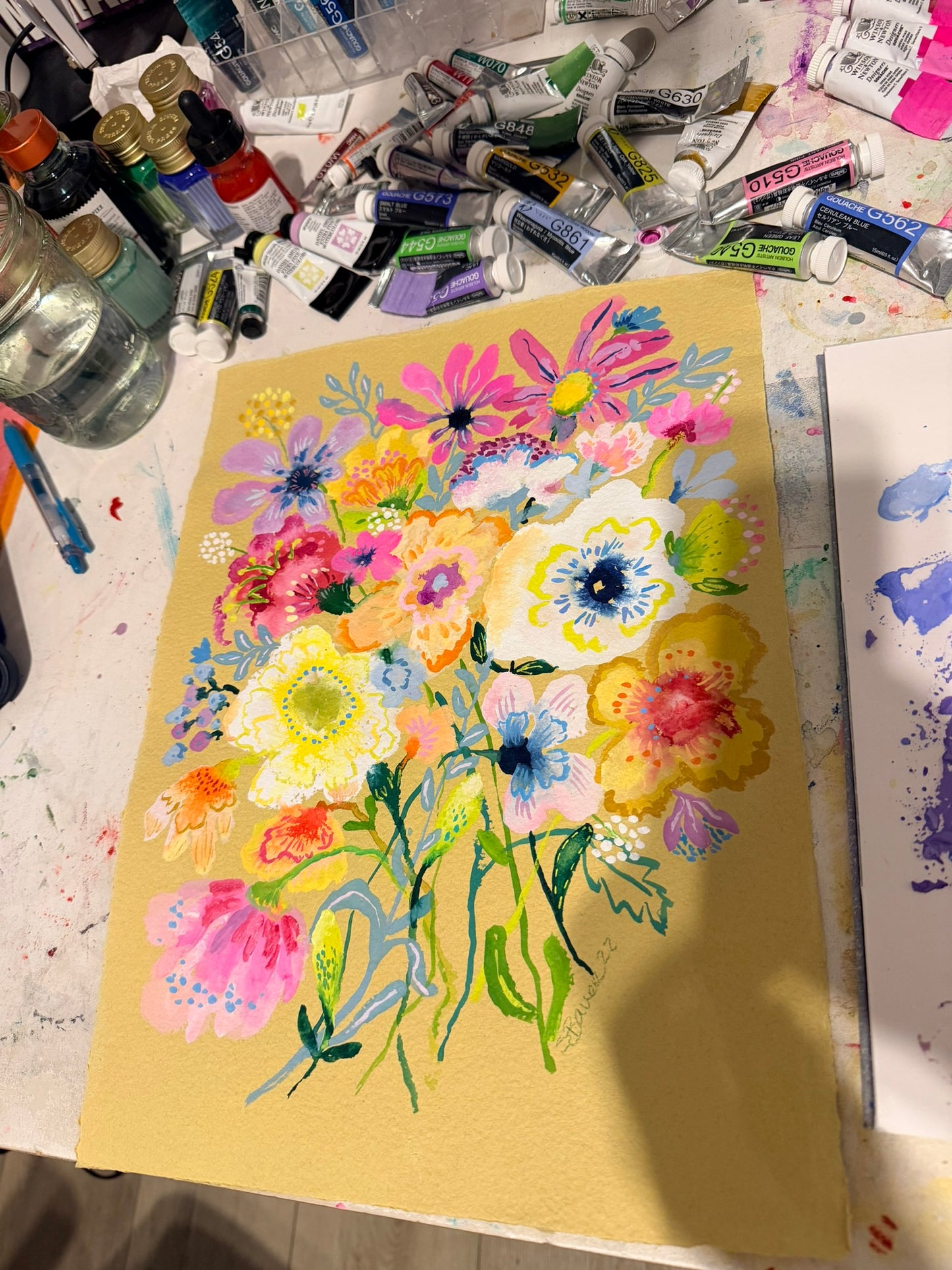 Colorful floral painting on a yellow background with art supplies around